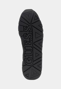 Suola di sneaker in gomma nera con motivi triangolari testurizzati e lettere "GUESS" in rilievo. Design resistente per trazione e grip.