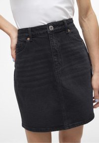 Svart denim minikjol med insvängd midja, framfickdetaljer, metallknappslutning och synlig textur från tygvävning.