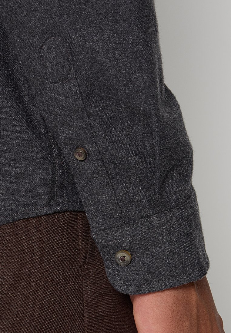 Graues Wollhemd mit strukturierter Oberfläche; mit Knopfmanschetten und dezenten Nähten. Nahaufnahme des Ärmels und der Manschette.