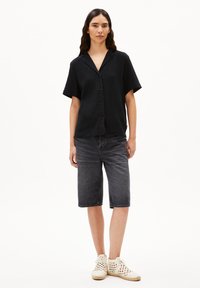 Zwarte kortarm button-up shirt van gestructureerde stof, gecombineerd met grijze denim Bermuda shorts en lichtgekleurde gevlochten schoenen.