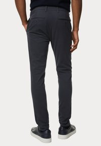 Pantaloni slim-fit grigi scuri con tasche posteriori, cuciture sottili e una texture liscia, abbinati a sneaker blu navy.