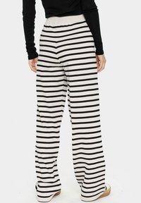 Pantalons à rayures noires et blanches, à jambes larges, avec une texture douce, une taille élastique et une coupe décontractée, associés à des chaussures de couleur claire.