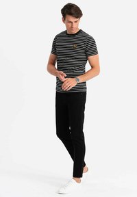 Černobíle pruhované tričko s kulatým výstřihem, spárované s černými kalhotami a bílými teniskami; jemný logotyp na hrudi.