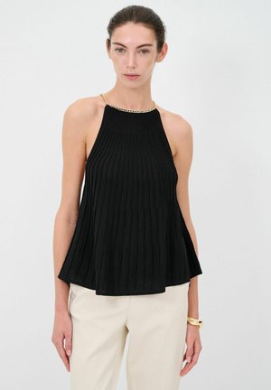 Haut noir à col halter avec des plis verticaux, présentant un col en chaîne dorée. Le tissu est léger et tombe doucement sous la taille.