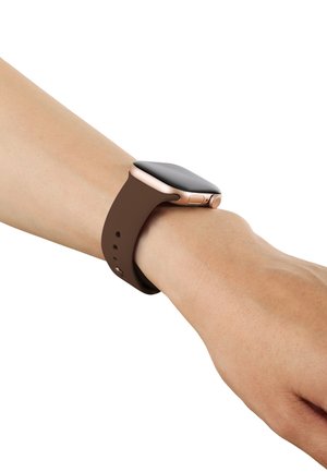 Polso con uno smartwatch nero con cassa in oro rosa e cinturino in silicone marrone su sfondo bianco.