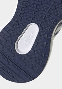Podeszwa buta Adidas o granatowej fakturze gumowej, z białym logo i różnorodnym wzorem bieżnika zapewniającym przyczepność. Widoczne rozmieszczone gumowe wypustki.