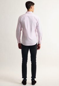 Camisa de botones rosa claro con mangas largas, cuello y un patrón sutil, combinada con jeans ajustados negros y zapatos marrones.