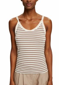Mujer que lleva una blusa sin mangas de rayas horizontales en beige y blanco, con bordes beige y un pequeño detalle de corazón en el pecho.