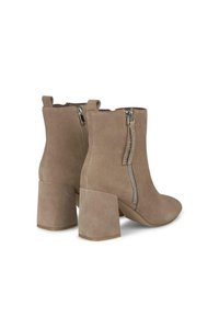 Botas de ante marrón hasta el tobillo con un tacón grueso, que presentan cremalleras laterales adornadas con pequeñas tachuelas. Textura suave y diseño de punta afilada.