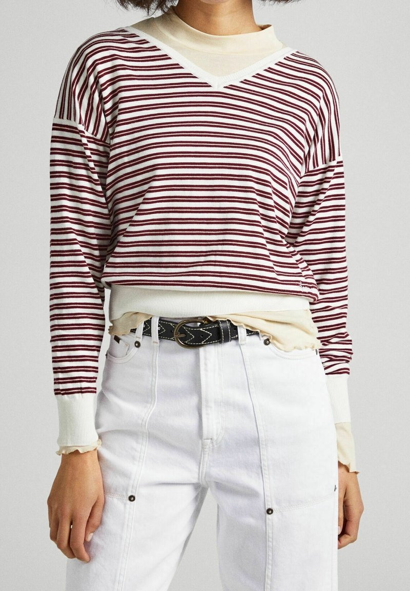 Pull-over rayé bordeaux et blanc, avec un col en V et des poignets côtelés, associé à un pantalon blanc taille haute et une ceinture noire.