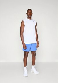 Valge varrukateta sportlik särk, sinised püksid ja valged vabaajajalatsid. Sile kangas, lõõgastav lõige, särgil minimaalne bränding.