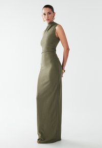 Robe sans manches vert olive avec un col montant, un corsage ajusté et un tissu texturé. Présente un détail de fronces sur le côté et une longueur maxi.