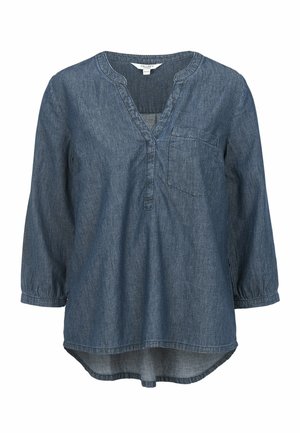 Denim-Tunika mit V-Ausschnitt, langen Ärmeln und einer aufgesetzten Tasche. Sie hat einen abgerundeten Saum und besteht aus einem weichen Stoff in einem mittleren Blauton.