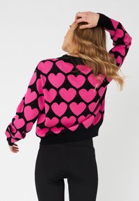 Maglione con motivo a cuori rosa su sfondo nero; presenta maniche lunghe e una vestibilità rilassata. Texture morbida e polsini a costine ai polsi.