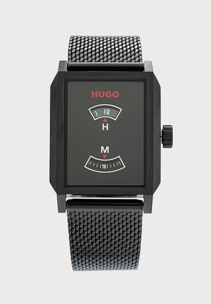 Montre digitale carrée noire avec bracelet en métal mesh, logo HUGO rouge, et fenêtres d'affichage courbées distinctes pour les heures et les minutes.