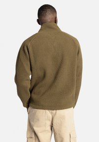 Pull en polaire vert olive, doté d'un col haut et d'un tissu texturé. Le dos présente un design épuré et sans couture.