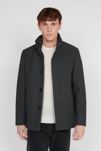 Grau wollener Mantel mit einem hohen Kragen, fünf großen schwarzen Knöpfen und einem geraden Schnitt, kombiniert mit einem hellen Pullover und dunklen Hosen.