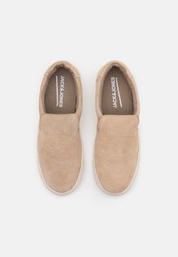 Beiget mokkasiinit, joissa sivuilla joustavat paneelit, pyöreä kärki ja pehmustettu sisäpohja. Sisäpuolella "JACK & JONES" -brändäys.