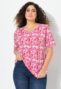 Hlavní části červená a bílá květinová vzorovaná halenka s krátkým rukávem a výstřihem do V, s uvolněným střihem a měkkou tkaninou. V kombinaci s tmavými džíny.