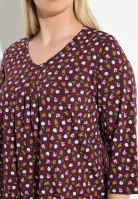 Blusa de manga corta en burdeos con escote en V, que presenta un estampado juguetón de muñecos de jengibre, tazas y huevos. Tejido suave con detalle fruncido.