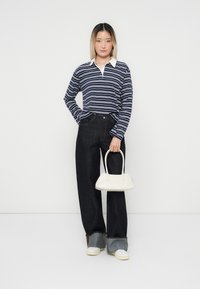 Marineblå og hvite striper på langermet polo, mørke, vide jeans og en liten hvit håndveske. Sneakers med et lagdelt mansjettblikk.