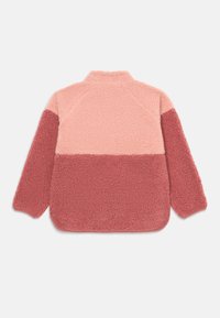 Meleg polárdzseki, világos rózsaszín és bordó színben, puha és bolyhos anyagból készült. Jellemzői a magas gallér és a hosszú ujjú kialakítás.