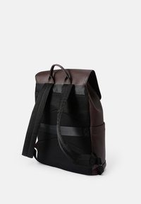 Mochila de cuero marrón con un respaldo de malla negra texturizada, que cuenta con correas ajustables negras y un asa superior para llevar.