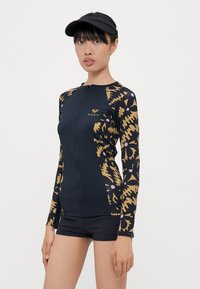 Long-sleeve rash guard with a front zipper, featuring a navy base and abstract gold and pink patterns on the sleeves. Paired with black shorts.