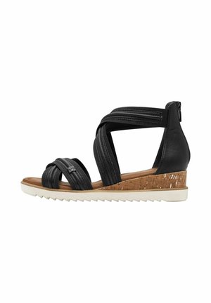 Sandali con zeppa nera, con cinturini incrociati, tomaia in pelle, soletta in sughero testurizzato, suola bianca seghettata e chiusura con cerniera sul retro.