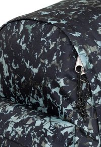 Zaino con stampa astratta nera e turchese, realizzato in tessuto resistente con superficie strutturata e spallacci regolabili, dettaglio con cursore della cerniera.