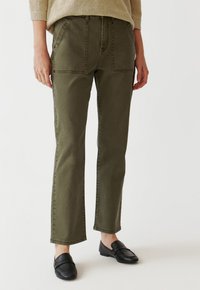 Olive vihreät suorat housut, joissa on etupaketaskut, näkyvät saumat ja sileä pinta, yhdistettynä mustiin loafer-kengiin.