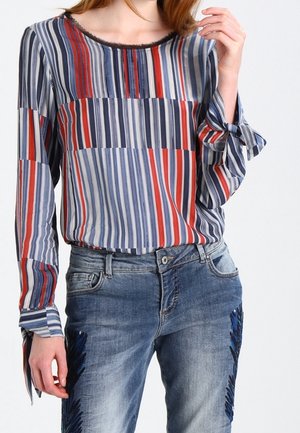 Blouse rayée à manches longues en marine, rouge et blanc avec un col rond et une coupe ample, associée à un jean bleu délavé avec des accents de franges bleues.