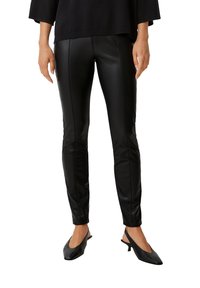 Czarne skórzane legginsy o dopasowanym kroju, z gładką fakturą i detalami szycia, w połączeniu z czarnymi, spiczastymi butami na słupku.