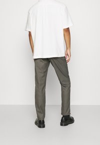 Biała koszula z krótkim rękawem w zestawieniu z szarymi spodniami w kratkę i czarnymi butami. Spodnie mają dopasowany krój i subtelny wzór w kratkę.