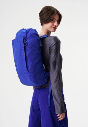 Blauer Rucksack mit abgerundetem Oberteil, Fronttasche und verstellbaren Trägern. Hergestellt aus strapazierfähigem Stoff mit runden Akzenten.