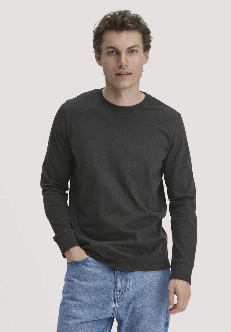 Langärmliges schwarzes Shirt aus Baumwolle, mit Rundhalsausschnitt und gerippten Bündchen. Getragen mit hellblauen Denim-Jeans.