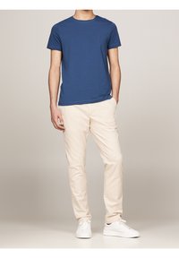 Camiseta de algodón azul de cuello redondo combinada con chinos de algodón beige y zapatillas blancas, mostrando un estilo simple y casual.