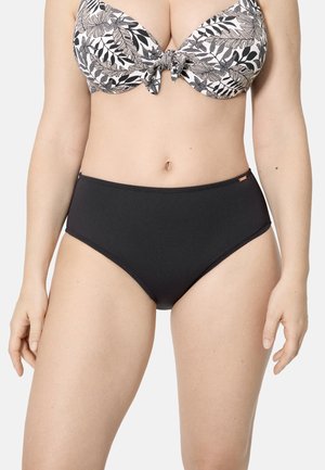 Mujer con un bikini de tiro alto negro y un top bikini con estampado de hojas en blanco y negro, con un nudo frontal.