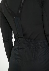 Mustat elastiset henkselit kiinnittyvät vastaavaan mustaan kankaaseen, jossa on rypistetty vyötärö. Pintakuvio on sileä ja istuva muotoilu.