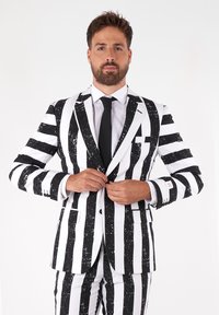 Čierno-biely pruhovaný oblek s lesklou textúrou. Má dvojité zapínanie, ostré klopy a bielu košeľu pod ním.