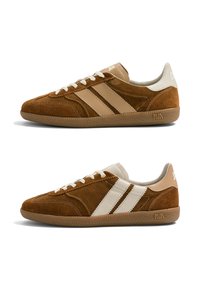Deux baskets en daim marron avec des lacets blancs et des bandes latérales blanches et beiges contrastées, montrées de côtés latéraux opposés.