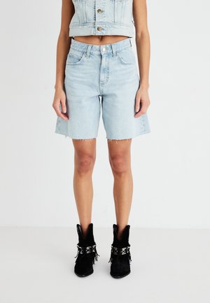Lyseblå denimshorts med rå kant, høy midje-design og frontlommer, kombinert med svarte semskede ankelstøvler med frynse detaljer.