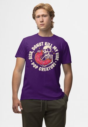 Fioletowy bawełniany t-shirt z grafiką czaszki trzymającej różowego pączka z lukrem i kolorową posypką oraz wyraźnym napisem.