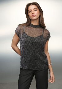 Must tekstuuriga top lühikeste varrukatega ja kõrge kaelusega. Omadus on läbipaistev pealiskate metallikniitidega, mis loob kihilise efekti.