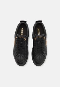 Sorte quiltede sneakers i kunstlæder med rund tå, polstret krave, sorte snørebånd og hardware i guld-tone. "GUESS" logo på indersålen.
