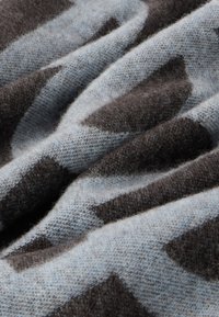 Tkanina z wełny w ciemnobrązowym i jasnoniebieskim kolorze o miękkiej fakturze, z delikatnymi falami i geometrycznym wzorem.