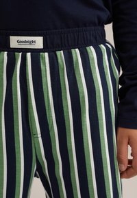 Pajama hlače s črtami imajo izmenične zelene, mornarsko modre in bele črte, z elastičnim pasom in oznako z napisom "Lahko noč." Mehka bombažna tekstura.