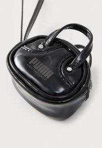 Small shiny black Puma pouch with handle and logo, resting on a white surface.