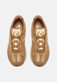Bruine sneakers met een bovenwerk van mesh en suède, voorzien van beige accenten, een ronde neus en vetersluiting. Logo op de tong en textuurdetails.