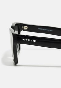 Mustad mustad prillid läikiva viimistlusega. Kindel raam kannab brändi "ARNETTE" valgete tähtedega külgedel.
